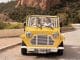 Moke électrique Mk2 jaune vue de face sur une route côtière, deux occupants